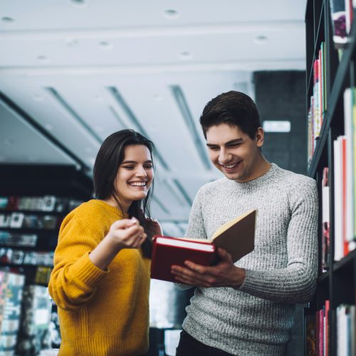 Happy young students choosing book in library